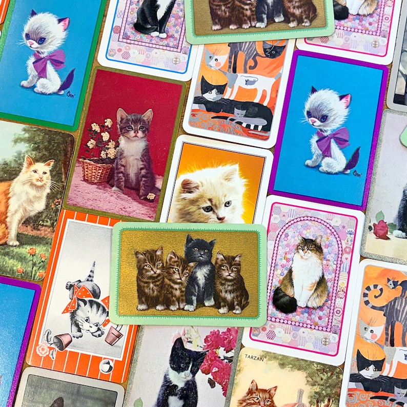 May include: A collection of vintage cat-themed playing cards. The cards feature various illustrations of cats in different poses and settings, with vibrant colors and a retro aesthetic. Some cards have a gold border.