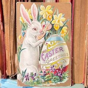 Cartolina della serie Conigli di Pasqua antichi, coniglietto bianco con tavolozza d'artista che dipinge un uovo colorato, fiori primaverili su biglietto d'auguri d'epoca
