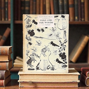 May include: A vintage book titled "Oaks and Oak Woods" by A.G. Tansley, part of the "Field Study Books" series. The cover features black and white illustrations of various insects, plants, and animals. The book is stacked on top of other books.