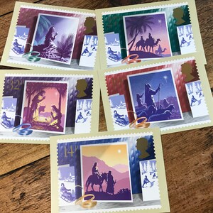 May include: A collection of five rectangular postage stamps featuring Christmas-themed illustrations in shades of purple, blue, and orange. Each stamp displays a central nativity scene, a silhouette of Queen Elizabeth II, and small winter vignettes.