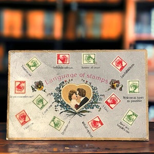 Carte postale ancienne en langue des timbres pour la Saint-Valentin, les amoureux encadrés par un coeur en or avec des pensées et des myosotis, lettres d'amour secrètes