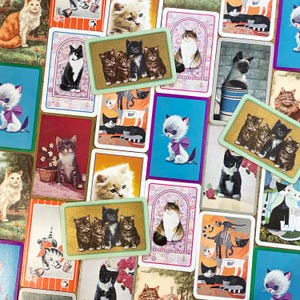 May include: A collection of vintage cat-themed playing cards. The cards feature various cat illustrations, including kittens with bows, black and white cats, and groups of kittens. The cards have a colorful, retro aesthetic, with a variety of backgrounds and designs.