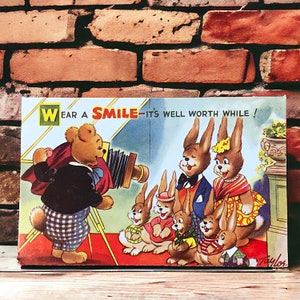 Tragen Sie eine Smile Vintage Postkarte von Arnold Taylor für Bamforth and Co, niedliche Häschen und einen Teddybären auf einer unbenutzten Karte der Merry Message Serie