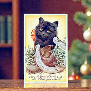 May include: A vintage-style rectangular postcard featuring a black cat with yellow eyes, a brown leather boot, a silver horseshoe, and green sprigs. The text reads: Here's Good Luck and all that goes with it! The background is a soft yellow gradient.