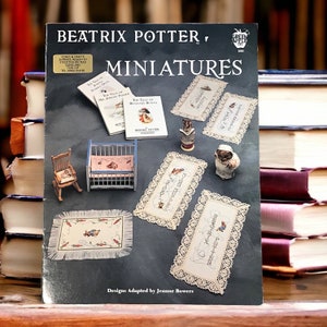 May include: A craft pattern book titled Beatrix Potter Miniatures by Green Apple Co. The cover features miniature items including small books, a wooden rocking chair, a crib, a fringed rug, and lace-trimmed embroidered samplers with character motifs.