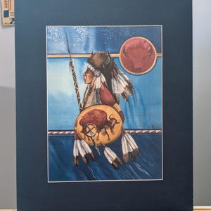 May include: Watercolor painting of a Native American figure in profile, holding a spear and shield. The shield features a bison image. The background is blue with a red circle. Feathers and traditional headdress are visible.