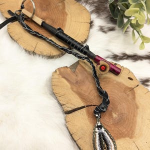 May include: Handmade beaded pendant necklace with a teardrop design in shades of white, black, and gray. The necklace features a braided black leather cord. A wooden key chain with black leather wrapping is also visible.