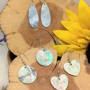 May include: Five pairs of earrings with silver hooks. Two pairs are teardrop-shaped, and the other three pairs are round and heart-shaped. The earrings have a pearlescent, iridescent finish, with colors of blue, green, and pink.