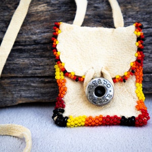 May include: A small, white leather pouch with a beaded border in red, orange, yellow, and black. The pouch has a silver button with the text "agapo" on it.