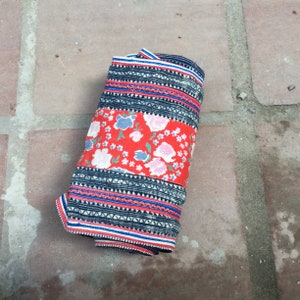 May include: A rolled up fabric with a red, white, and blue floral pattern. The fabric has a black and white geometric pattern on the edges.