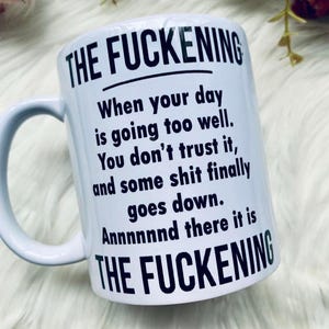 May include: White ceramic mug with the text "THE FUCKENING" at the top and bottom. The body of the mug has the following text: "When your day is going too well. You don't trust it, and some shit finally goes down. Annnnnnd there it is."