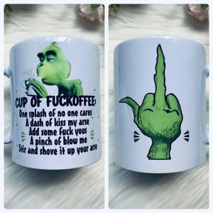 May include: White ceramic mug featuring a green Grinch graphic on one side, holding a cup and smoking. The other side shows a green hand giving the middle finger. Text on the mug reads "CUP OF FUCKOFFEE" with humorous instructions.