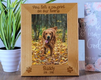 May include: A wooden picture frame with a photo of a golden retriever dog in a forest. The frame has a paw print design and the inscription "You left a pawprint on our hearts" and "Buddy 2018-2020".