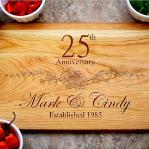 May include: A wooden cutting board with a personalized inscription. The inscription reads "25th Anniversary Mark & Cindy Established 1985".