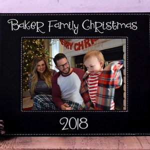 May include: Black leather picture frame with white stitching and the text "Baker Family Christmas 2018". The frame has a photo of a family of three in front of a fireplace.