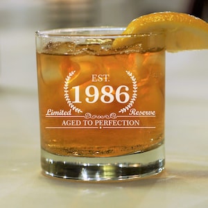 May include: A clear glass with ice and a lemon wedge. The glass has the text "EST. 1986 Limited Reserve Aged to Perfection" etched on the side.