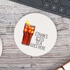 May include: White round coaster with a drawing of a glass of iced tea with a lemon wedge. The text "ETHAN'S ICED TEA GOES HERE" is printed in black.