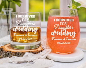 May include: Two clear glass tumblers with the text "I survived my daughter's wedding" and the date "08.22.2023". One tumbler is a standard glass and the other is a wine glass.