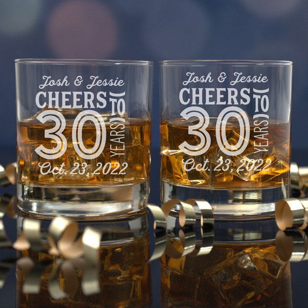 May include: Two clear glass tumblers with the text "Josh & Jessie Cheers to 30 Years Oct. 23, 2022" etched on the front. The glasses are filled with amber liquid and ice cubes.