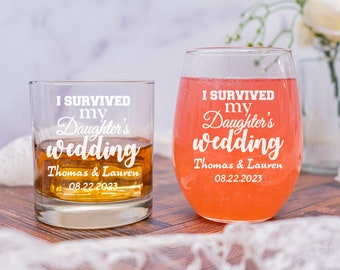 May include: Two clear glass tumblers with the text "I survived my daughter's wedding" and the names "Thomas & Lauren" and the date "08.22.2023". The tumbler on the left is filled with a brown liquid and the tumbler on the right is filled with a pink liquid.