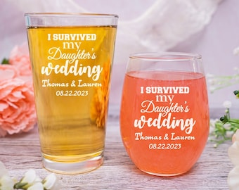 May include: Two clear glass beverage containers with the text "I survived my daughter's wedding" and the names "Thomas & Lauren" and the date "08.22.2023". The container on the left is a pint glass and the container on the right is a wine glass.
