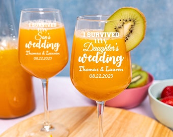 May include: Two clear glass wine glasses with orange juice. The glasses are engraved with the text "I survived my Son's wedding" and "I survived my Daughter's wedding". The text also includes the names "Thomas & Lauren" and the date "08.22.2023".