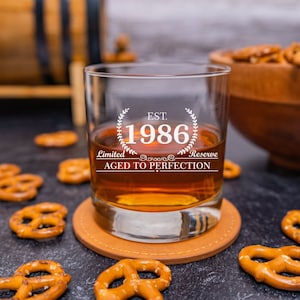 May include: A clear glass with a brown liquid inside. The glass has a white design that says "EST. 1986 Limited Reserve Aged to Perfection".