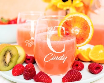 May include: Two stemless wine glasses with personalised names, "Tiff" and "Cindy", featuring floral designs. The glasses are filled with a pink drink and surrounded by fruit, including raspberries, kiwi, and orange slices.
