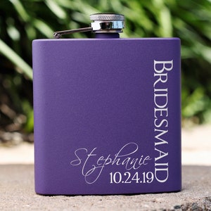May include: Purple metal flask with a silver top and the words "BRIDESMAID" and "Stephanie 10.24.19" engraved on the front.