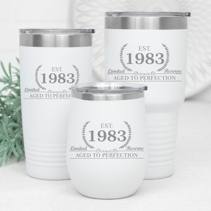 May include: Three white insulated tumblers with silver lids. Each tumbler has the text "EST. 1983" inside a laurel wreath, with "Limited Reserve Aged to Perfection" below. The tumblers are different sizes.