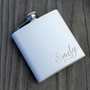 May include: White metal flask with a silver cap and the name "Emily" engraved on the front.