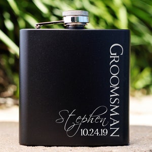 May include: Black metal flask with a silver lid and engraved text that reads "Groomsman Stephen 10.24.19".