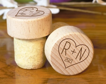 Può includere: Due tappi per bottiglie in legno con fondo in sughero. Ogni tappo presenta un design a forma di cuore con le iniziali "R+N" e l'anno "2021" inciso sulla parte superiore.