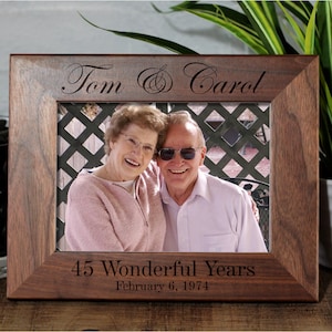 May include: A dark brown wooden picture frame with a photo of an older couple. The frame is engraved with the names "Tom & Carol" and the text "45 Wonderful Years February 6, 1974".