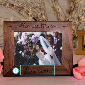 May include: A dark brown wooden picture frame with a white mat and a photo of a bride and groom. The frame is engraved with "Mr & Mrs Lawson" and a heart.