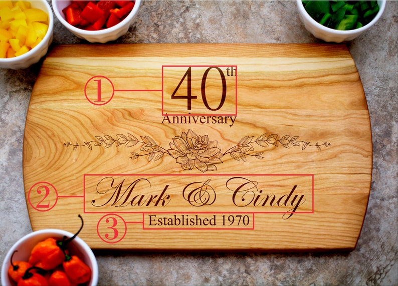 May include: A wooden cutting board with a floral design engraved on it. The board is personalized with the text "40th Anniversary", "Mark & Cindy", and "Established 1970".