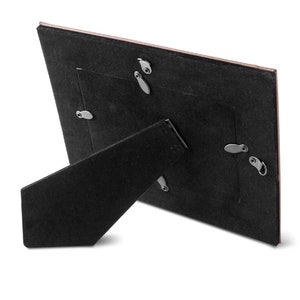 May include: Black picture frame with a brown backing and a stand on the back. The frame has a small opening for a picture.