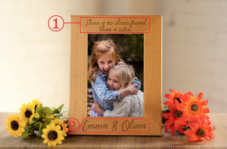 May include: A wooden picture frame with a photo of two young girls hugging. The frame has an inscription that reads "There is no closer friend than a sister." and the names "Emma & Olivia" are engraved below the photo.