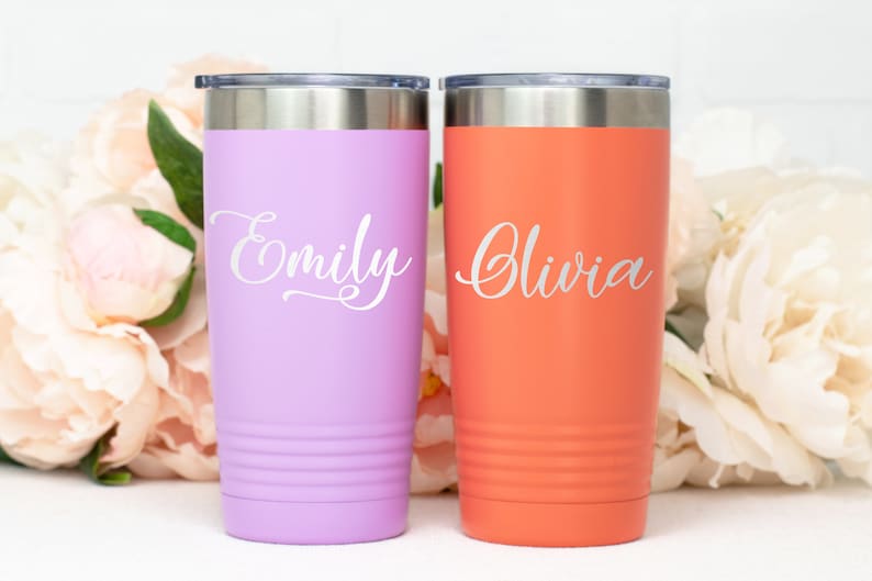 Puede incluir: Dos vasos de acero inoxidable personalizados, uno lavanda y otro naranja, con los nombres "Emily" y "Olivia" grabados en blanco.