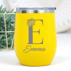 K&ouml;nnte beinhalten: Gelber Edelstahl-Weinglas mit einem Blumendesign und dem Buchstaben "E" auf der Vorderseite graviert. Der Name "Emma" ist unter dem Buchstaben graviert.
