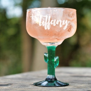 Op de afbeelding: Een groen glazen margarita-glas met een cactussteel en -voet. Het glas is gevuld met een roze drankje en ijs. Het glas is gepersonaliseerd met de naam "Tiffany".