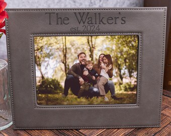 May include: A gray leather picture frame with a stitched border. The frame has a photo of a family of four in a park. The text "The Walker's est. 2024" is engraved on the frame.