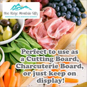 May include: A wooden serving board with a variety of food items, including olives, green beans, carrots, prosciutto, blueberries, and strawberries. The board is perfect for serving a charcuterie board or as a cutting board. The text "Perfect to use as a Cutting Board, Charcuterie Board, or just keep on display!" is printed on the board.