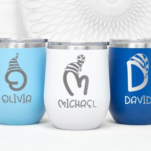 May include: Three personalized stainless steel wine tumblers with blue, white, and blue lids. The tumblers are engraved with the names Olivia, Michael, and David, each with a stylized letter and a Christmas hat design.