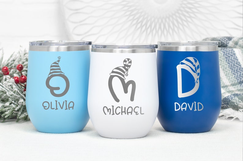 May include: Three personalized stainless steel wine tumblers with blue, white, and blue lids. The tumblers are engraved with the names Olivia, Michael, and David, each with a stylized letter and a Christmas hat design.
