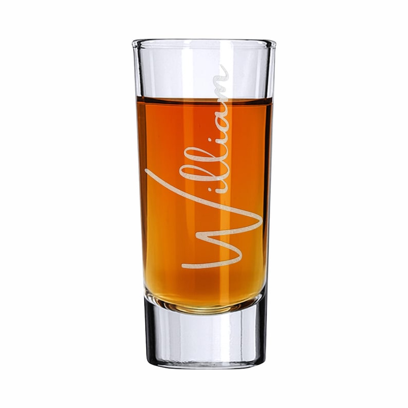 Op de afbeelding: Een helder shotglaasje gevuld met amberkleurige vloeistof. De naam "William" is in sierlijke letters op de voorkant gegraveerd. Het glas heeft een dikke bodem en een rechte, cilindrische vorm.