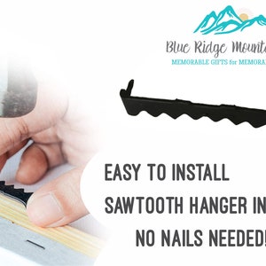 May include: A black sawtooth hanger being installed on a canvas frame with a hammer. The image includes the text "EASY TO INSTALL, SAWTOOTH HANGER INCLUDED, NO NAILS NEEDED!" and the logo for Blue Ridge Mountain Gifts.