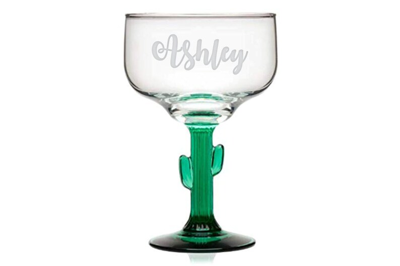 Op de afbeelding: Een helder glazen margarita-glas met een groene cactussteel en -voet. Het glas is gegraveerd met de naam "Ashley".