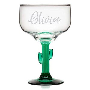 May include: A clear glass margarita glass with a green cactus stem and base. The glass is engraved with the name "Olivia".