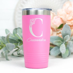 K&ouml;nnte beinhalten: Rosafarbener Edelstahlbecher mit einem wei&szlig;en Blumenmuster und dem Buchstaben "C" sowie dem Namen "Cassandra" auf der Vorderseite.